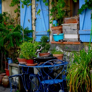 Tables, chaises, plantes en pot devant un mur de pirres et fenêtres à volets bleus - France  - collection de photos clin d'oeil, catégorie rues